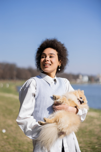 pleased african american woman holding in arms pomeranian dog - Foto, Imagem
