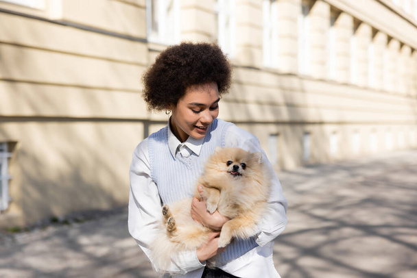 veselý africký americký žena držení pomeranian pes na ulici - Fotografie, Obrázek