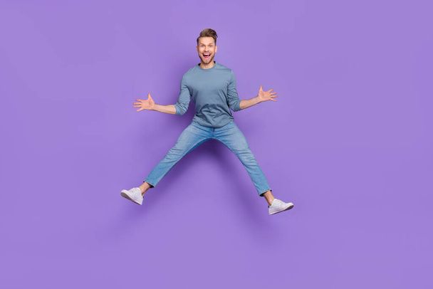 Photo of excited impressed guy wear grey shirt jumping high like star isolated violet color background - Foto, Imagem