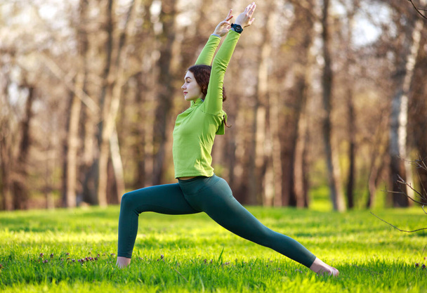 Young woman yogi in park on the green grass doing fitness exercises stretching the body, healthy lifestyle in pure nature - Foto, imagen