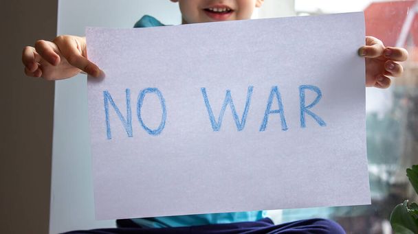 Маленький мальчик держит в руках листок бумаги, на котором написано "нет войне". селективный фокус - Фото, изображение