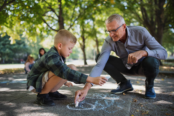 Grandfather with grandson drawing with chalks on pavement outdoors in park. - Zdjęcie, obraz