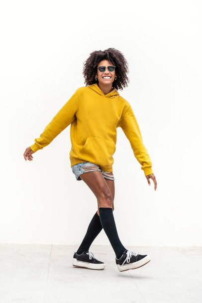 Cheerful female skater with afro hairstyle dancing and smiling to the camera. Girl wearing fashionable clothes. A lot of copy space - Foto, afbeelding