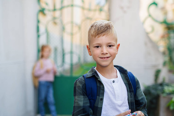 Happy little schoolboy looking at camera in front of school. - Foto, Imagen