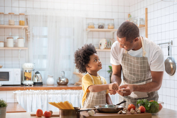 Happy Black African American Father and little son cooking together in kitchen. Brazilian Single dad and Afro boy with smiling face. - Фото, изображение