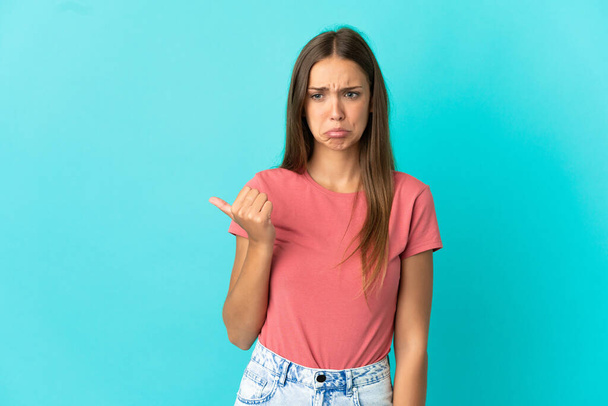 junge Frau über isoliertem blauen Hintergrund unglücklich und zur Seite zeigend - Foto, Bild