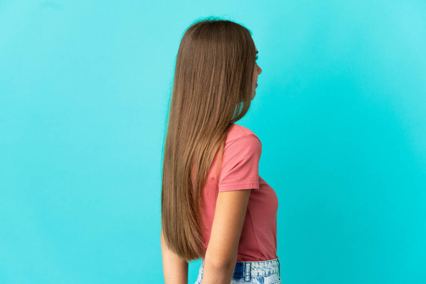 Junge Frau vor isoliertem blauen Hintergrund in Rückenlage und rückblickend - Foto, Bild