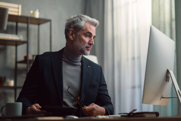 Mature businessman working on computer indoors in office. - Photo, Image