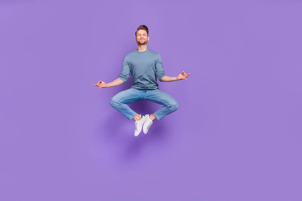 Photo of charming dreamy guy dressed grey shirt jumping high practicing yoga isolated purple color background - Foto, Imagem