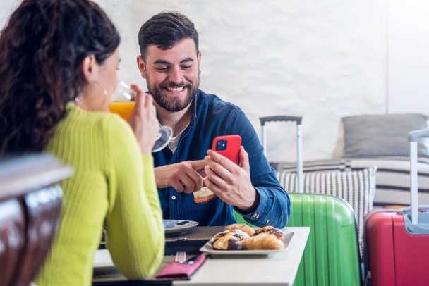 Tourist couple looking at the phone and having breakfast in a hotel restaurant - Valokuva, kuva