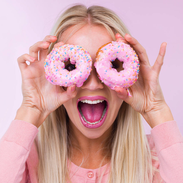 Τρελαίνεται για Ντο-NUTS. Τραβηγμένο πλάνο μιας γυναίκας που κρατάει ντόνατς μπροστά στα μάτια της ενώ είναι απομονωμένη σε ροζ.. - Φωτογραφία, εικόνα