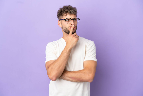 Delivery caucasian man isolated on purple background having doubts while looking up - Photo, Image