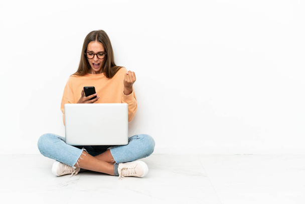 Fiatal nő egy laptop ül a padlón meglepve, és üzenetet küld - Fotó, kép