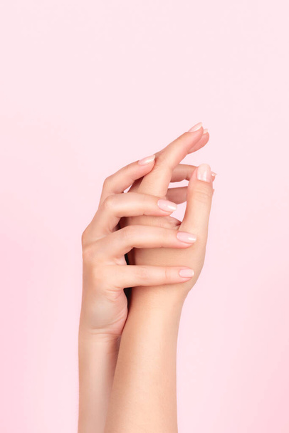 Female hands with beautiful natural manicure - pink nude nails on pink background. Nail care concept - Photo, Image
