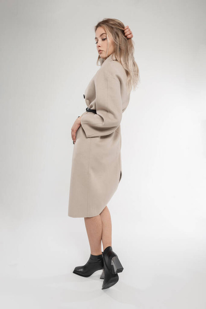 Beautiful young blonde girl in fashionable spring outwear with fashion coat and stylish black leather shoes posing in the studio. Women's new collection of shoes - Valokuva, kuva