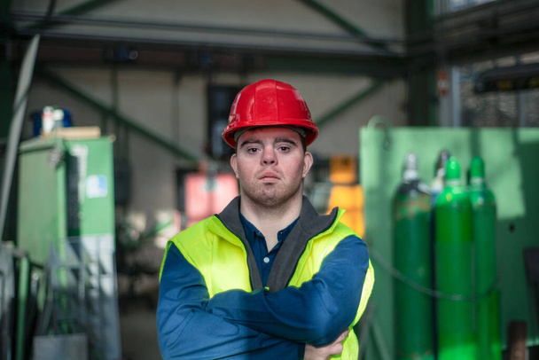 Young man with Down syndrome working in industrial factory, social integration concept. - Фото, изображение