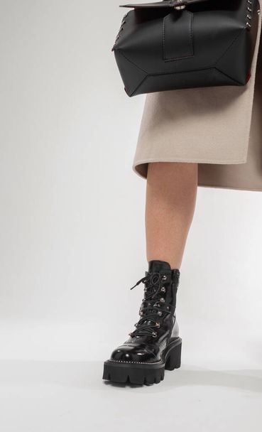 Menina elegante em um casaco elegante com sapatos de couro preto vintage e uma bolsa em um fundo branco. Perna de mulher em sapatos na moda, close-up - Foto, Imagem