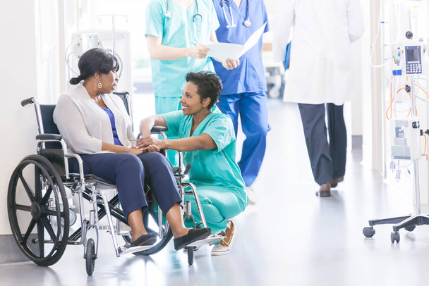 Paciente de silla de ruedas femenina afroamericana étnica con personal profesional de enfermería especialista en el corredor del centro de recuperación del hospital - Foto, Imagen