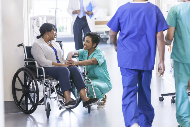 Caring African American female nurse in hospital uniform scrubs with wheelchair patient in medical centre - Fotoğraf, Görsel