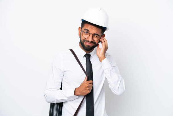 Young architect Brazilian man with helmet and holding blueprints isolated on white background frustrated and covering ears - Photo, Image