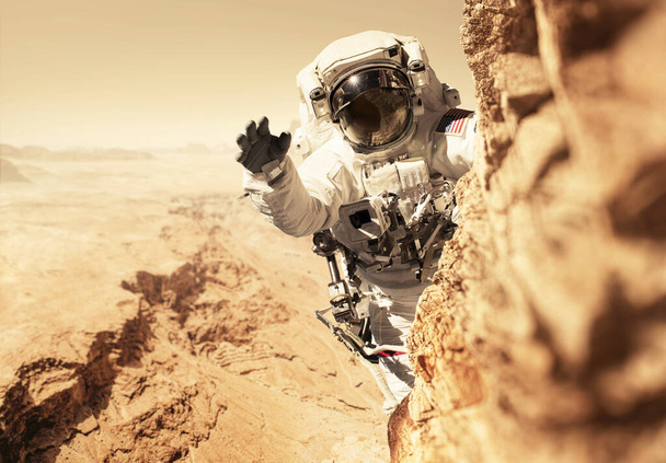 Астронавт Марсианин летит на красную планету и поднимается на гору на скале. Космический человек завоевывает и населяет новую планету Марс. Планета Марс и люди, концепция. Добро пожаловать в новый дом  - Фото, изображение