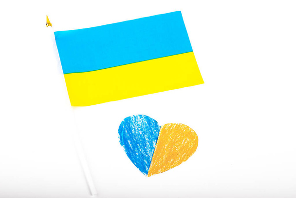 Флаг Украины на белом фоне и бумажное сердце, окрашенное в цвет флага Украины. Символ государства. Лежать, лежать. Принято. Патриотические штучки. Национальный вымпел - Фото, изображение