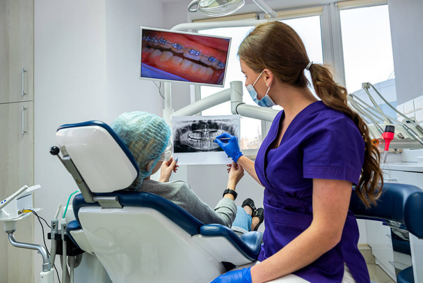 Ένας επαγγελματίας οδοντίατρος δείχνει στον ασθενή φωτογραφίες από το σαγόνι και τα δόντια του. Η έννοια των εικόνων της γνάθου και των δοντιών στον οδοντίατρο - Φωτογραφία, εικόνα