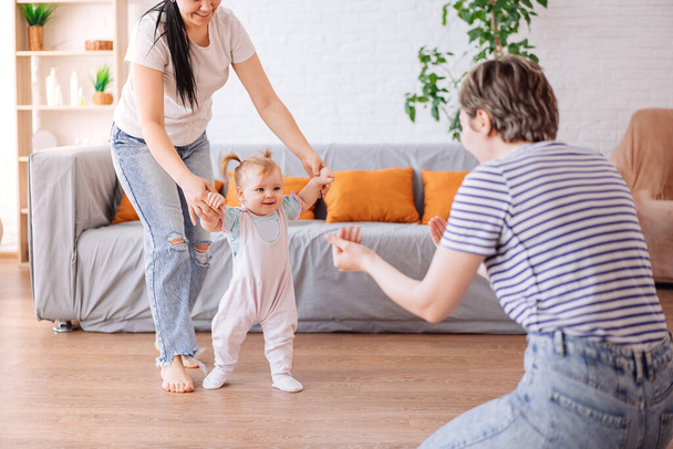 a little girl takes her first steps with the help of her parents. lesbians. The concept of a happy family - Фото, зображення