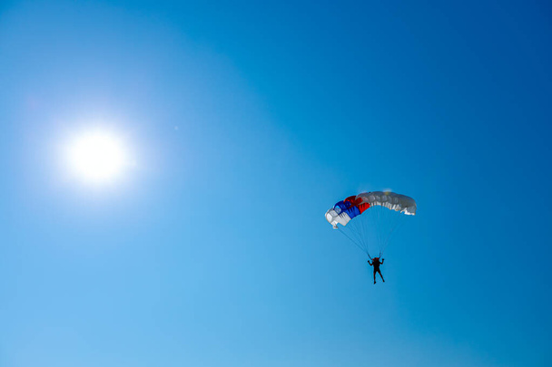 Parachutist is flying slowly down with an open parachute. Skydiving, gliding, parachute jump - Photo, Image