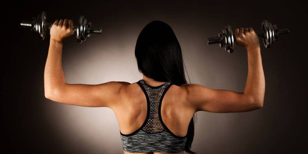 Aktive junge Frau turnt mit Kurzhanteln in Fitnessstudio - Foto, Bild