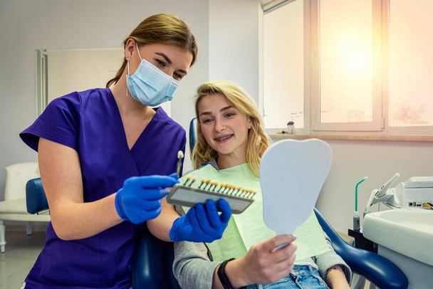fiatal specialista fogorvos nő speciális ruhák mutat paletta fogszín egy női beteg. Fogfehérítés koncepciója - Fotó, kép