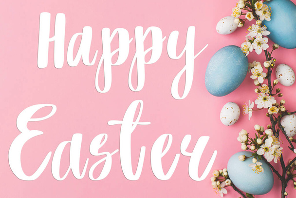 Happy Easter greeting card. Happy Easter text and modern stylish easter eggs and flowers flat lay on pink background. Seasons greeting card, handwritten lettering - Fotografie, Obrázek