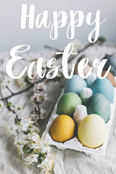 Happy Easter greeting card. Happy Easter text and stylish colorful Easter eggs and cherry blossoms on rustic table. Seasons greeting card, handwritten lettering - Foto, immagini