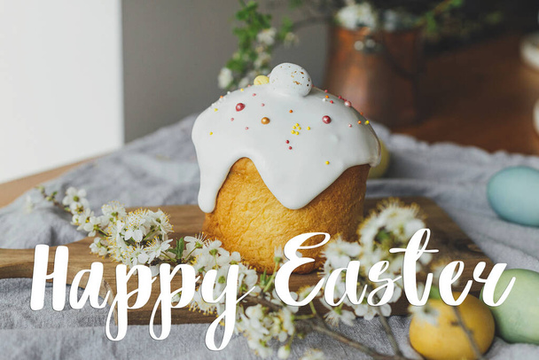 Happy Easter greeting card. Happy Easter text and stylish easter bread, natural dyed eggs and spring blossom on rustic table. Seasons greeting card, handwritten lettering - Photo, image