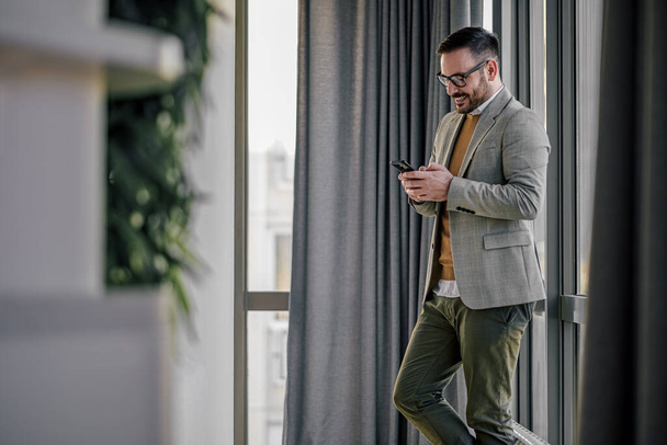 Confident adult man, typing a text, while standing in the office lobby. - Foto, Bild