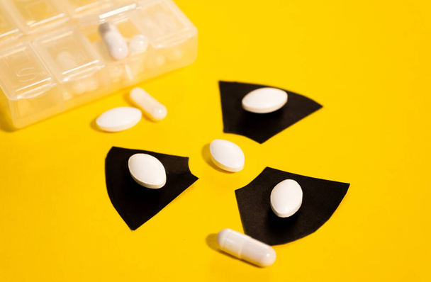 Multiple anti-radiation pills based on iodine on a yellow background and the radiation warning sign - Foto, afbeelding