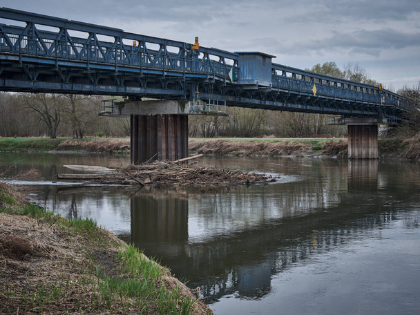 Blaue Metallbrücke über den Fluss Morava mit Treibholz auf einer Säule, Slowakei - Foto, Bild
