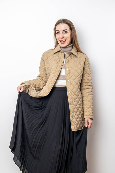 Smiling young woman in a jacket midi skirt against a white wall  - Foto, afbeelding