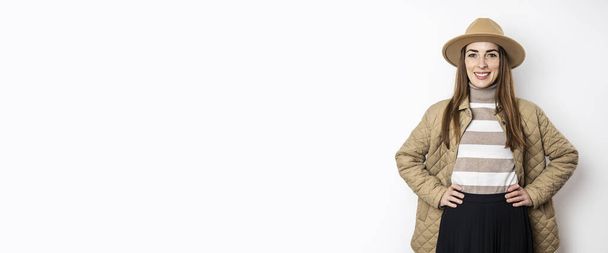 Улыбающаяся молодая женщина в пиджаке в шляпе у белой стены. Баннер - Фото, изображение