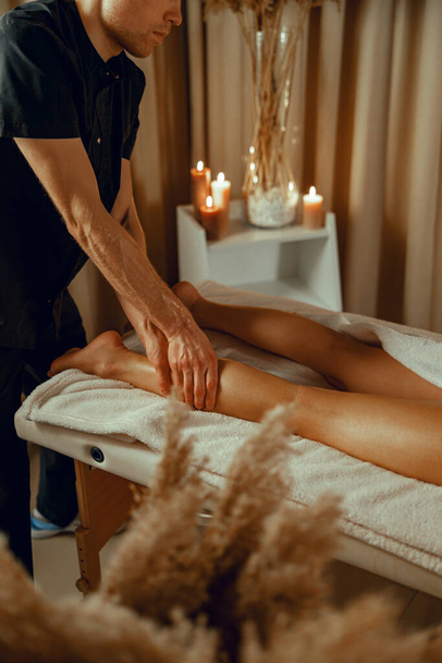Concentrated male therapist doing professional leg massage for female client at spa center - Фото, изображение