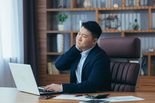 Tired young asian businessman man, worker holding his neck, feeling body aches at work in office - Foto, Imagen