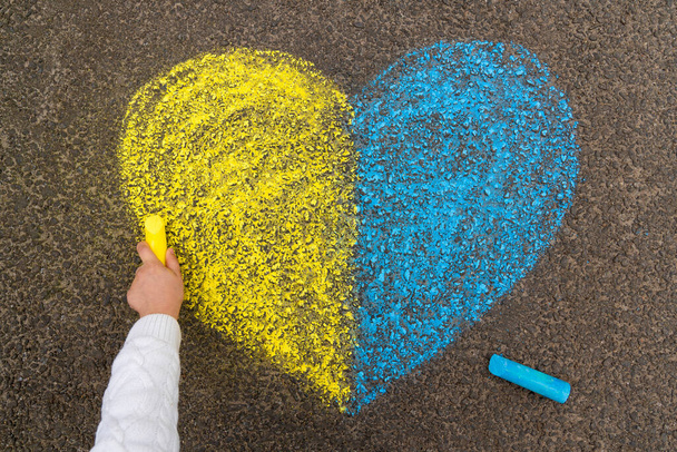 La main d'un enfant dessine un cœur avec des crayons sur le trottoir avec les couleurs patriotiques nationales ukrainiennes de jaune et de bleu. Arrêtez la guerre en Ukraine. Photo de haute qualité - Photo, image