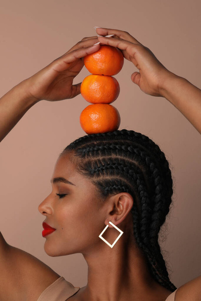 Vertikální portrét africké mladé ženy pózuje s pomeranči na hlavě na bílém - Fotografie, Obrázek