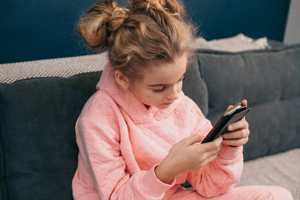 Koulutyttö katsomassa videota älypuhelimella mobiili. Muotokuva pikkutyttö käyttää älypuhelinta istuessaan sohvalla. Elämäntyylin suunnitteluun. Etäopetus - Valokuva, kuva