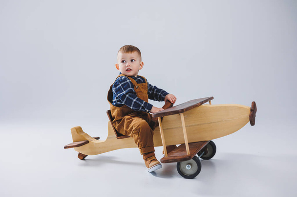 Kareli gömlekli 3 yaşında bir çocuk büyük tahta bir uçakta oturuyor. Çocuklar için ağaçtan yapılmış çevre dostu oyuncaklar. - Fotoğraf, Görsel