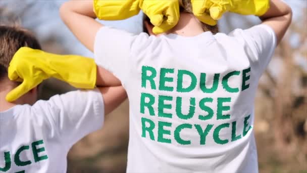 Jungen und Mädchen in Gummihandschuhen mit den Öko-Aufschriften auf ihren T-Shirts. Plastik-Müllabfuhr auf einer verschmutzten Lichtung - Filmmaterial, Video