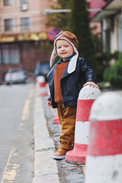 Stylowy 3-latek w skórzanej kurtce i brązowych spodniach spaceruje ulicą. Nowoczesne dziecko. Dziecięca moda. Szczęśliwe dziecko - Zdjęcie, obraz