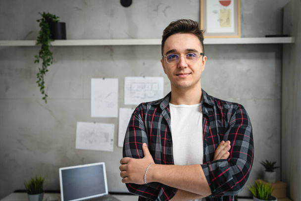 One confident man caucasian male entrepreneur or student standing in front of the desk ar home or work looking to the camera with arms crossed real people copy space half length happy smile - Fotoğraf, Görsel