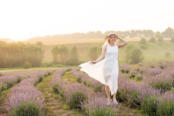 Krásná mladá žena kráčí po levandulovém poli. Módní šaty, slaměný klobouk. - Fotografie, Obrázek