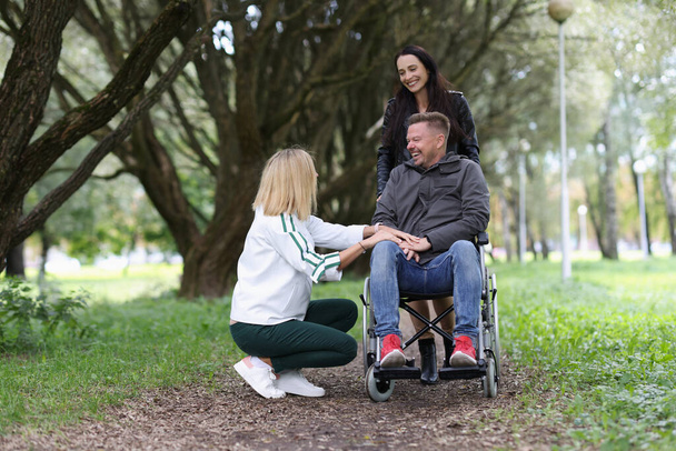Две женщины и мужчина в инвалидном кресле разговаривают в парке - Фото, изображение